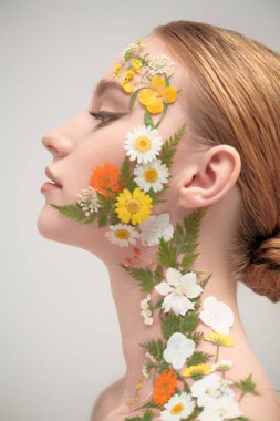 Çekici kızıl saçlı, zarif makyajlı ve yüzünde ve omzunda yaz çiçekleri olan bir kızın yakın çekimi. Beyaz arka plan. Kozmetik ve parfüm. Yazın kokusu..