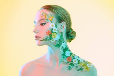 Zarif makyajlı ve yüzünde yaz çiçekleri olan güzel, genç bir kadının portresi. Açık pembe arka plan. Parfüm. Çiçek kokuları. Makyaj ve kozmetik. 