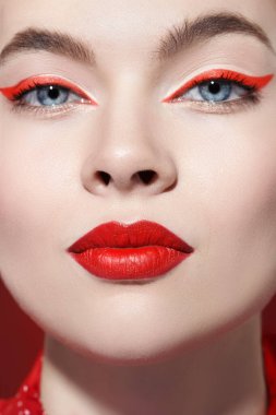 Sevimli kırmızı renk. Gözlerinde parlak kırmızı oklar ve kameraya bakan muhteşem kırmızı rujlu güzel bir kız modelin portresi. Makyaj ve makyaj malzemeleri. Yakın çekim..