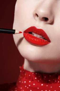 Makyaj ve makyaj malzemeleri. Güzel, parlak kırmızı rujlu bir mankenin dudaklarını kaplamak için kırmızı bir dudak kalemi sürerken çekilmiş görüntüsü. Yakın çekim..