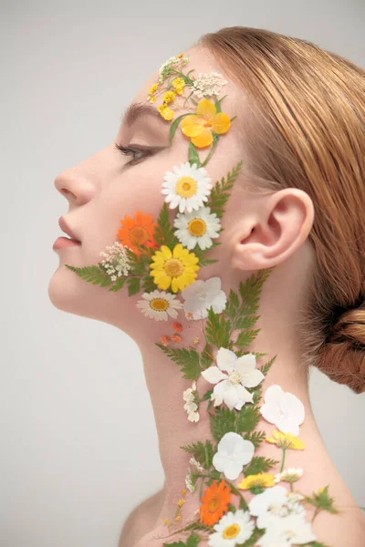 Çekici kızıl saçlı, zarif makyajlı ve yüzünde ve omzunda yaz çiçekleri olan bir kızın yakın çekimi. Beyaz arka plan. Kozmetik ve parfüm. Yazın kokusu..