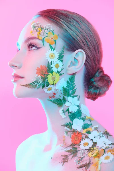Yüzünde zarif makyajı ve yaz çiçekleri olan güzel kızıl saçlı genç bir kadın profilde poz veriyor. Pembe arka plan. Parfüm. Makyaj ve makyaj malzemeleri. Güzellik ve çiçekler.