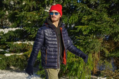 Güneşli bir kış gününde yürümek. Kış kıyafetleri içinde yakışıklı, kendine güvenen esmer bir adam kış parkında yürüyüş yapıyor. Kış modası.