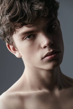 Kahverengi dalgalı saçlı, gömleksiz genç bir adamın stüdyo portresi. Erkek güzelliği ve sağlığı. Yakın çekim..