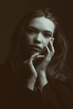 İnsanlar ve duygular. Siyah gömlekli, uzun kahverengi saçlı güzel bir kızın portresi kameraya sakince ve düşünceli bir şekilde bakıyor. Siyah ve beyaz çekim.