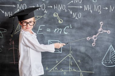 Zeki çocuklar. Beyaz gömlekli ve gözlüklü şirin bir kızın portresi. Elinde öğretmen iğnesi ve kimyasal formüllerle tahtada duruyor. Eğitim. 