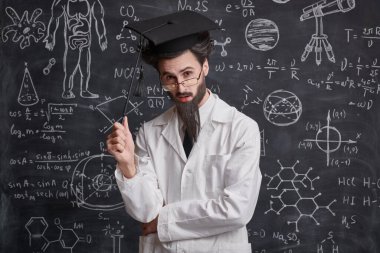 Bilim ve eğitim. Zeki, hevesli bir profesör, elinde bir işaret, elinde diyagramlar ve bilimsel formüllerle karatahtanın önünde duruyor ve kameraya bakıyor.. 