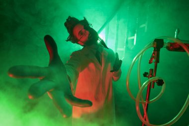 Bilim kurgu. Karanlık laboratuarında elini kameraya uzatarak gizemli yeşil ve kırmızı ışıkla aydınlanan takıntılı bir profesörün portresi..