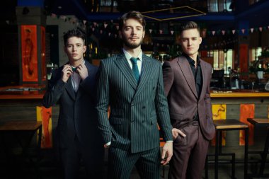 Erkek modası. Üç yakışıklı şık takım elbiseli bir restoranda birlikte poz veriyorlar.. 