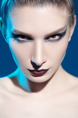 Kozmetik ve makyaj malzemeleri. Koyu renk agresif makyajlı güzel bir kadın modelin yakın çekimi. Mavi arkaplanda stüdyo resmi. 