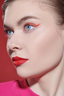 Güzellik konsepti. Zarif makyajlı çekici sarışın bir kız başka tarafa bakıyor. Kırmızı arka plan. Makyaj ve kozmetik. 