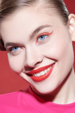 Makyaj ve makyaj malzemeleri. Parlak kırmızı rujlu güzel bir sarışın kız ve kırmızı arka planda büyüleyici bir şekilde gülümseyen kırmızı okları var. Güzellik konsepti.