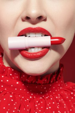 Sevimli kırmızı renk. Parlak kırmızı ruju olan güzel bir kız modelin portresi. Dişlerinde kırmızı ruj olan bir tüp. Makyaj ve makyaj malzemeleri. Yakın çekim.. 