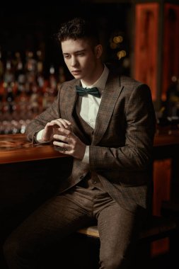 Şık takım elbiseli ve papyonlu çekici bir esmer adam bir restoranın barında oturmuş viski içiyor. İş adamı. Lüks yaşam tarzı.