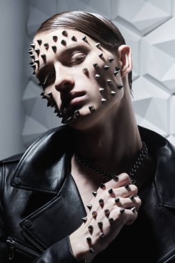 Rock tarzı ve moda. Siyah deri ceketli, yüzünde ve kolunda metal sivri uçlu beyaz bir arka planda vahşi bir gencin portresi..