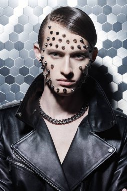 Agresif bir moda. Siyah deri ceketli, metalik teknoloji arka planında metal çiviler olan vahşi bir gencin portresi..