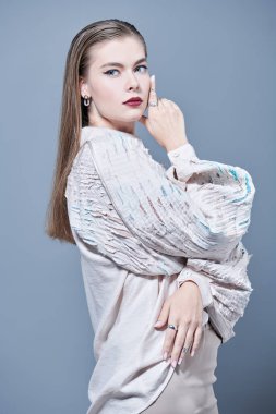 Mücevher ve yüksek moda. Zarif özel tasarım bluz ve değerli mücevherlerle poz veren güzel bir kadın modelin portresi. Makyaj ve saç stili. Gri arkaplanda stüdyo portresi. 