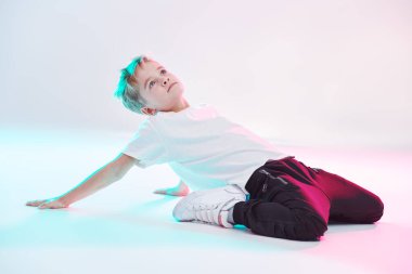 Stüdyoda dans eden havalı break dansçı çocuk beyaz arka planda karışık renkli ışıkta dans ediyor. Spor ve aktiviteler. Modern dans stili. Hip-hop dansçısı. 