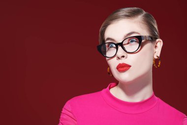 Parlak makyajlı, şık gözlükleri olan zarif sarışın bir kız şarap rengi bir arka planda poz veriyor. Makyaj ve makyaj malzemeleri. Gözlük stili. 