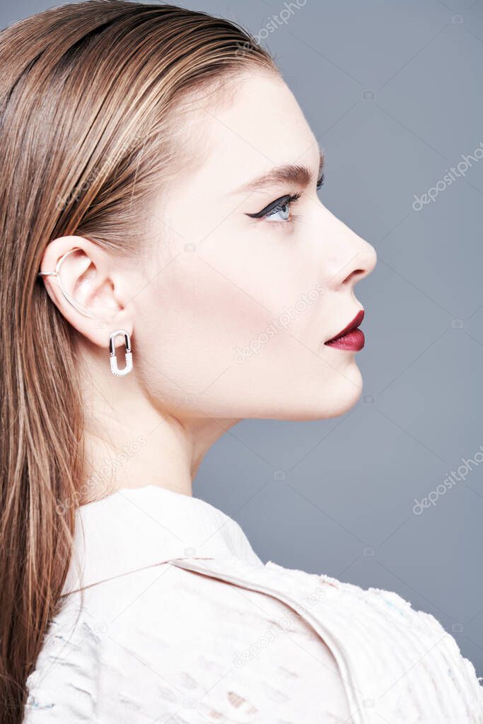 Beautiful female model posing in profile in an elegant haute couture blouse and bright makeup on her face. Make-up and hairstyle. Sideview portrait. High fashion shot. 