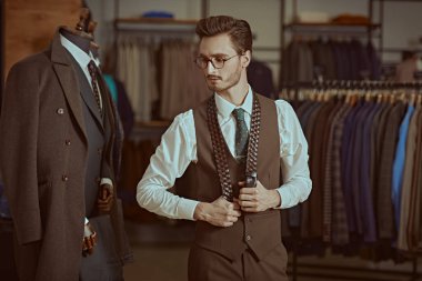 Yakışıklı kahverengi takım elbiseli saygıdeğer bir esmer adamın portresi şık kemerli bir erkek giyim mağazasında duruyor. Erkeklerin iş modası.