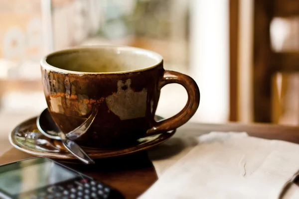 Tasse und Smartphone auf Holztisch im Café — Stockfoto