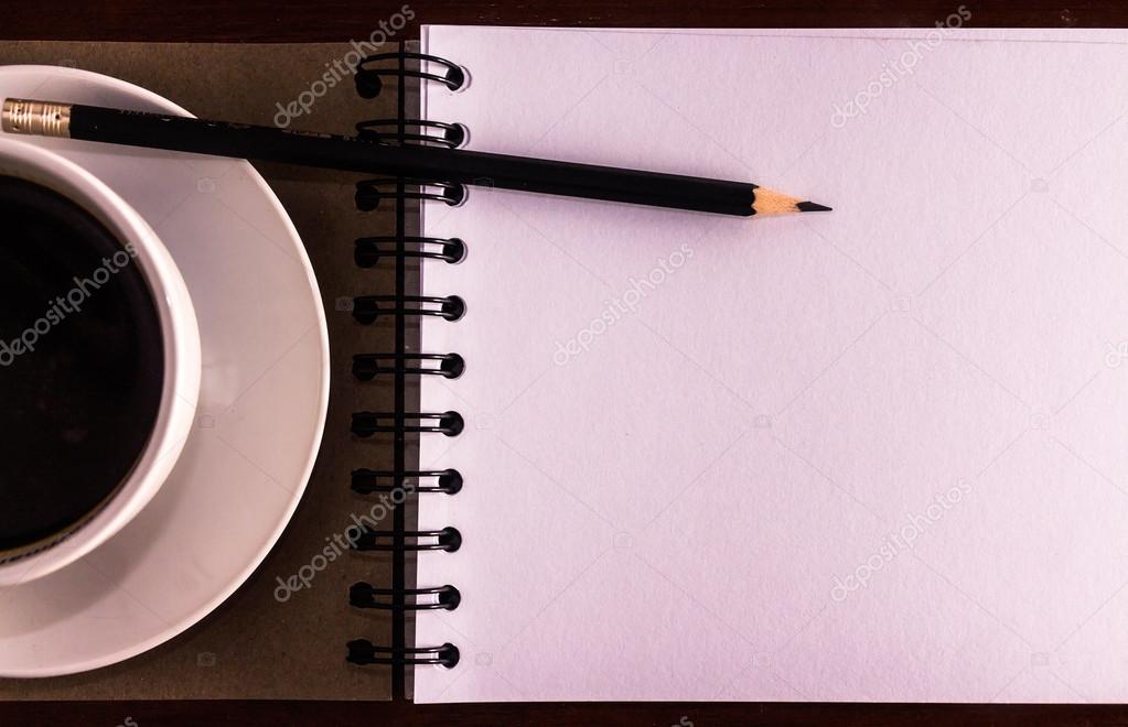 Open a blank white notebook, pencil and cup of coffee on the des
