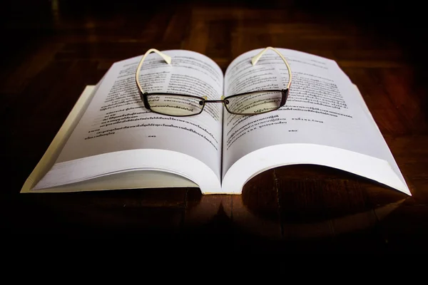 Ανοιχτό βιβλίο και γυαλιά στο γραφείο. — Φωτογραφία Αρχείου