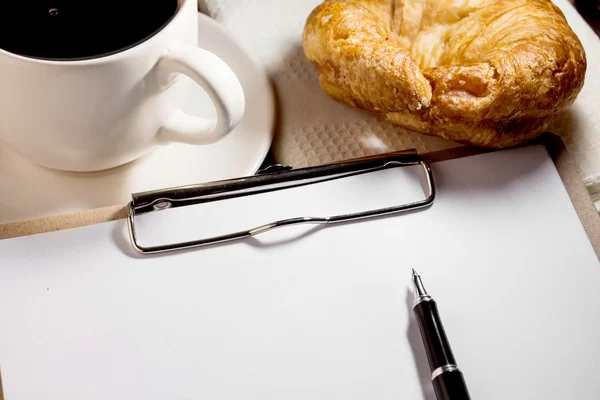 Blank white notebook, pen, cup of coffee and croissant on the de — стоковое фото