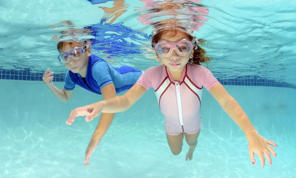 Dos niños nadando bajo el agua en la piscina — Foto de Stock