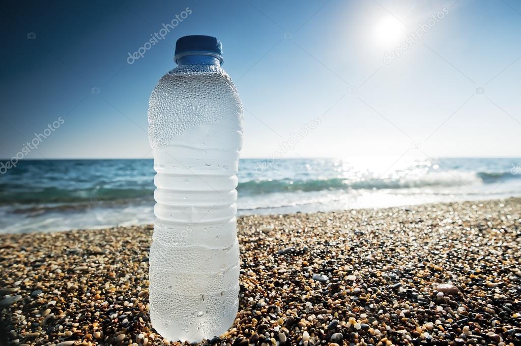 Bottle of fresh water is on the sand by the sea.