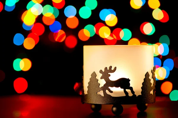 Bulanık ışıklar çelenk arka plan üzerine bir geyik figürü ile şamdan. — Stok fotoğraf