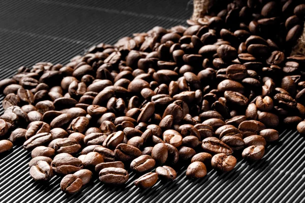 Coffee beans scattered on a black grooved — Stock Photo, Image