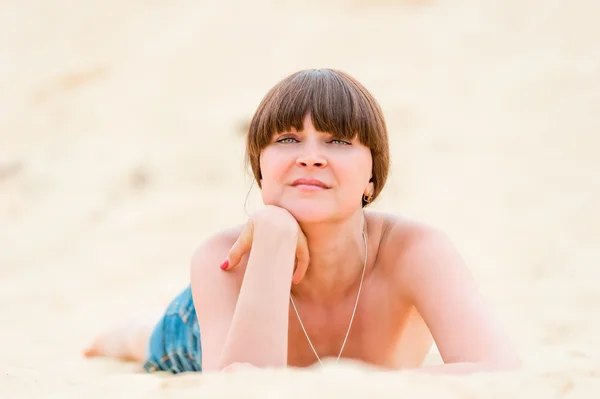 Chica en pantalones cortos de mezclilla bronceado mientras está acostado en la arena . — Foto de Stock