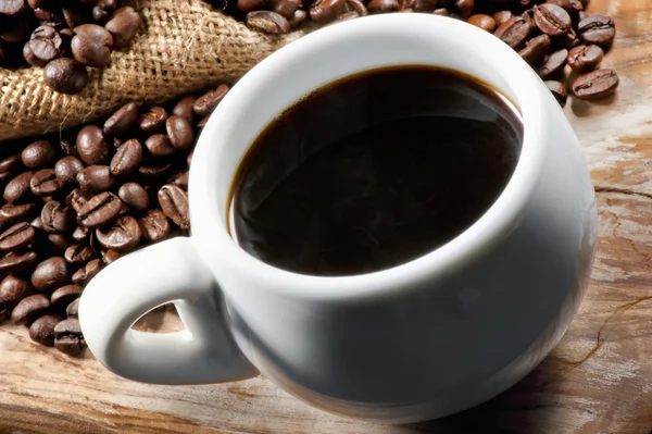 Taza blanca de café en una tabla de madera con granos de café dispersos —  Fotos de Stock