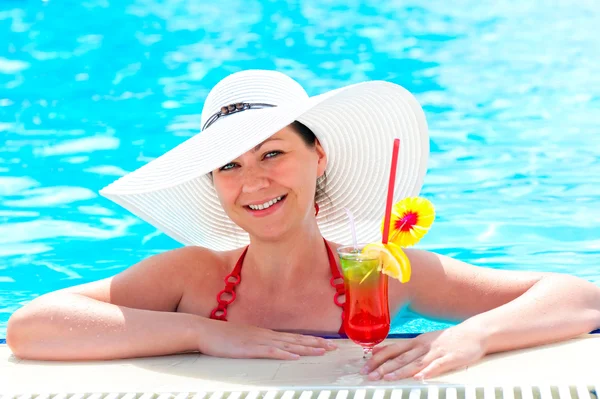 Donna in piscina con un cocktail in cappello bianco — Foto Stock