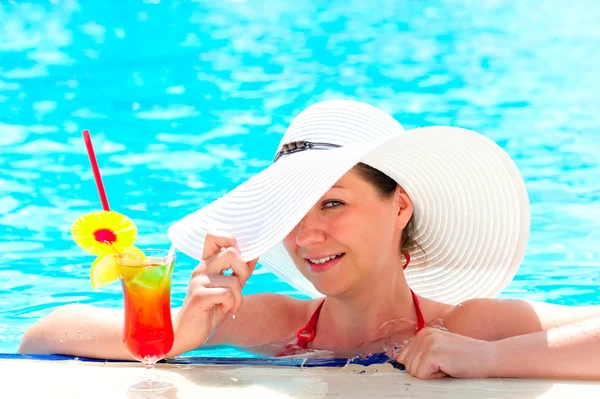 Chica feliz con un cóctel en la piscina sosteniendo una mano sombrero —  Fotos de Stock