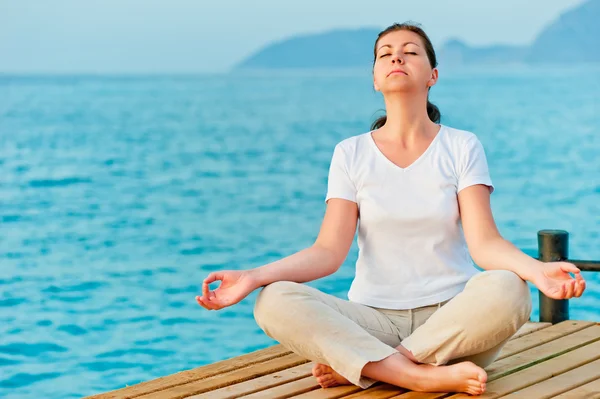 Girl sitting on a pier in the lotus position Royalty Free Stock Images