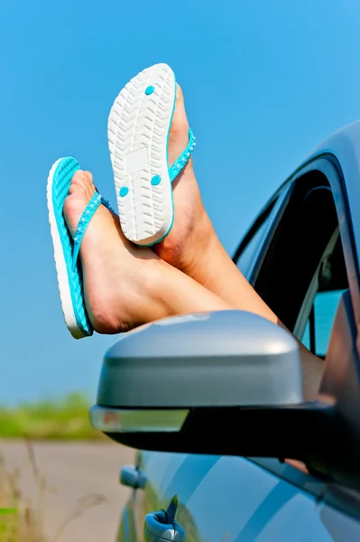 Pernas femininas penduradas na janela do carro aberto nos xistos — Fotografia de Stock