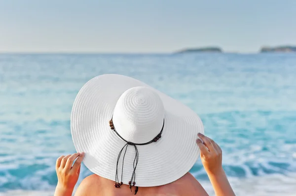 Une femme bronzant sur une chaise longue sur la plage et tenant le chapeau des mains — Photo