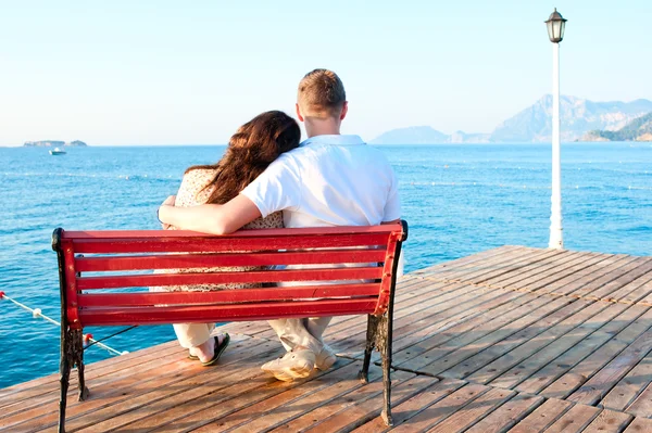 Casal amor sentado em um banco junto ao mar abraçando — Fotografia de Stock