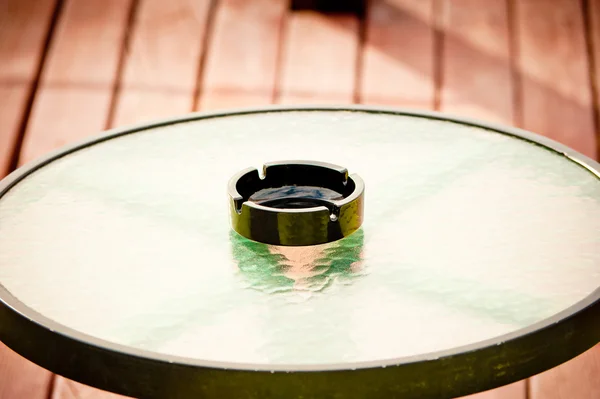 Cinzeiro vazio preto fica no meio de uma mesa de vidro redonda — Fotografia de Stock