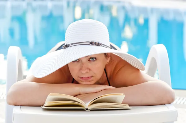 Mujer tumbada en una tumbona con un libro y tomando el sol cerca de la piscina —  Fotos de Stock