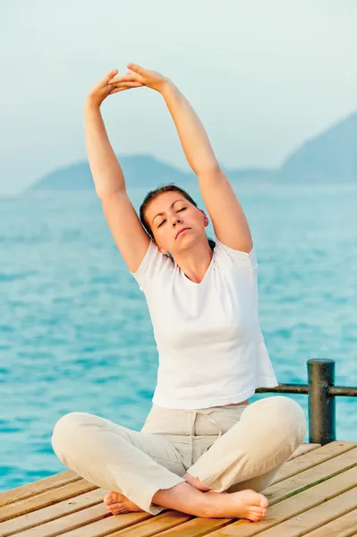 Schöne Frau, die sich morgens auf einem Steg am Meer dehnt — Stockfoto