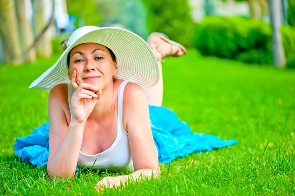Jente ligger på en grønn plen i en hvit hatt – stockfoto