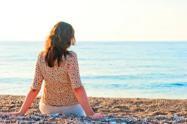 Mujer admirando el mar mientras se sienta en una playa de guijarros —  Fotos de Stock