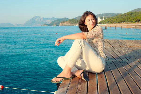 Tjejen sitter på en brygga vid havet och tittar åt sidan — Stockfoto