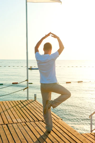 Mens staande op een pier op één been en houdt het evenwicht — Stockfoto