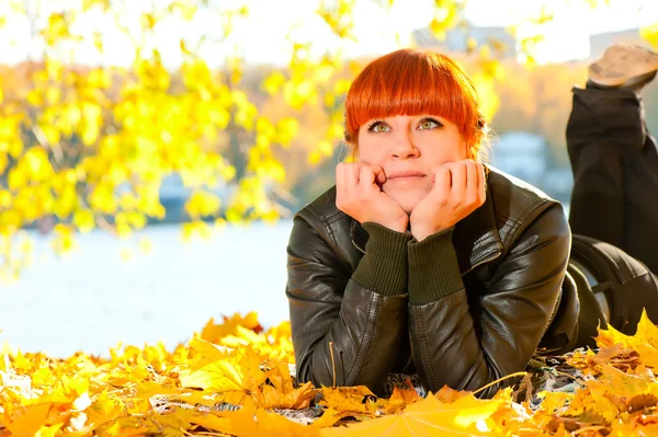 Beautiful girl with red hair in leaves in autumn park — Stock Photo, Image