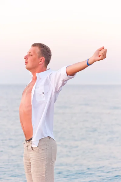 Bare-chested man stretching on sea background — Stock Photo, Image